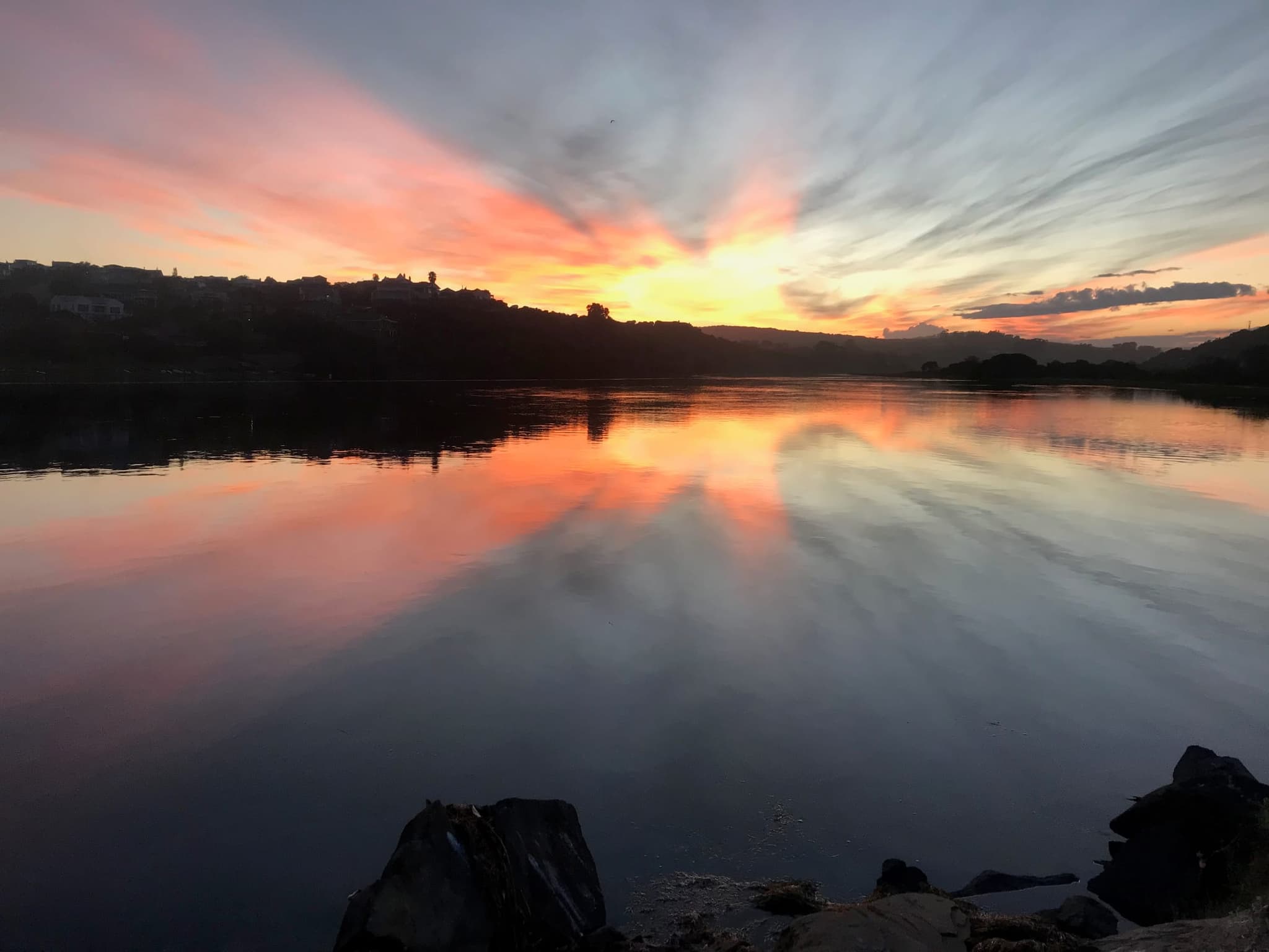 The Goukou River at sunset, the pink and orange sky mirrored on still water between dark wooded banks.