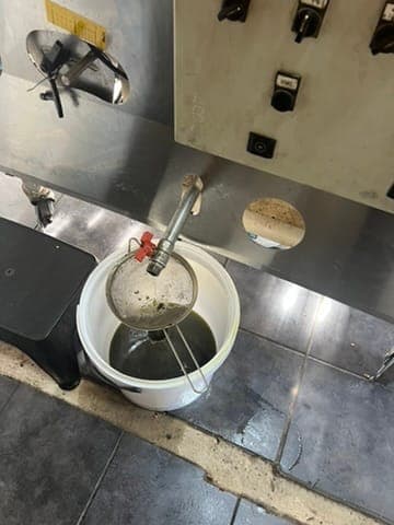 New olive oil running from the press into a bucket in the farm press room.