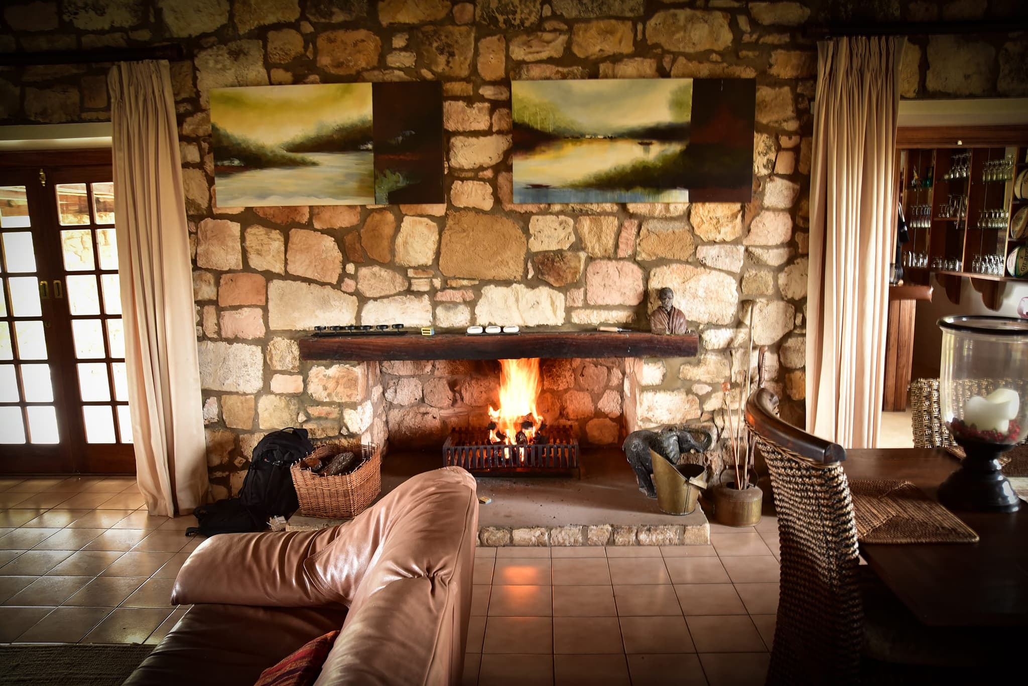 The Stonehouse lounge with a fire burning in a stone fireplace, leather sofas and paintings on the stone wall.