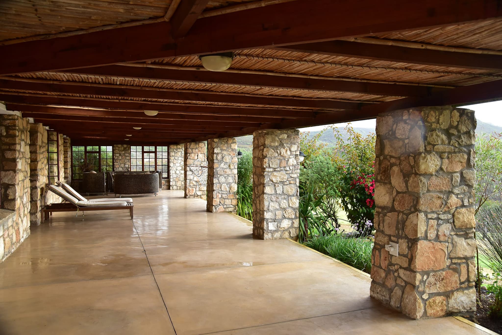 The long covered veranda of Stonehouse Lodge: stone pillars, a reed ceiling and loungers looking over the valley.