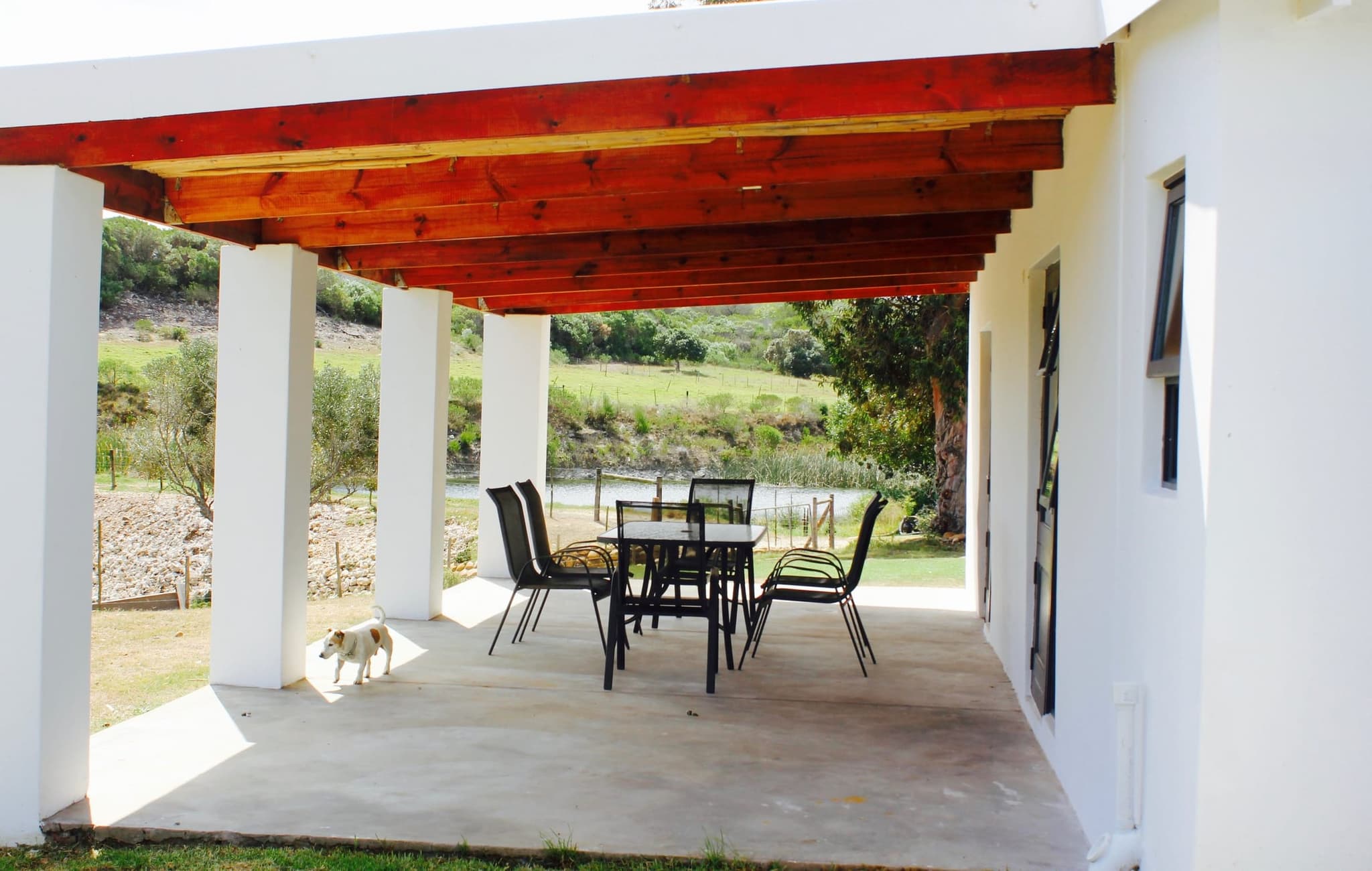 The covered veranda of White House Cottage with a red timber ceiling, a dining table and a view of the river.